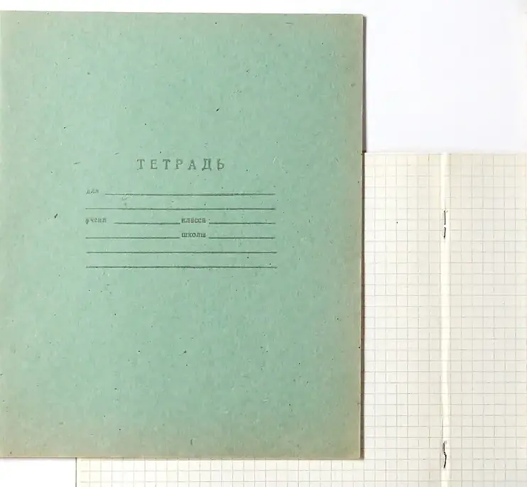A pale green school notebook beside open pages of squared paper
